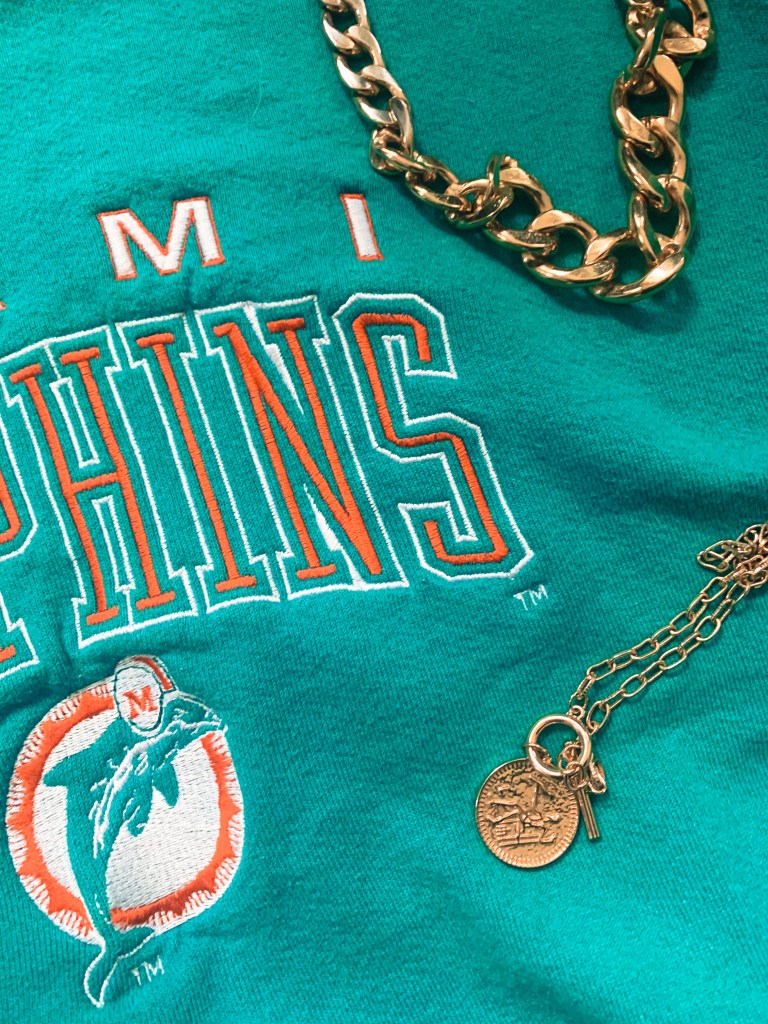 Closup of miami dolphins sweatshirt with gold necklaces